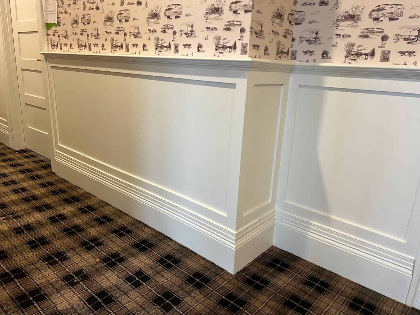 Close-up of custom wall paneling and trim molding with plaid carpet flooring and patterned wallpaper